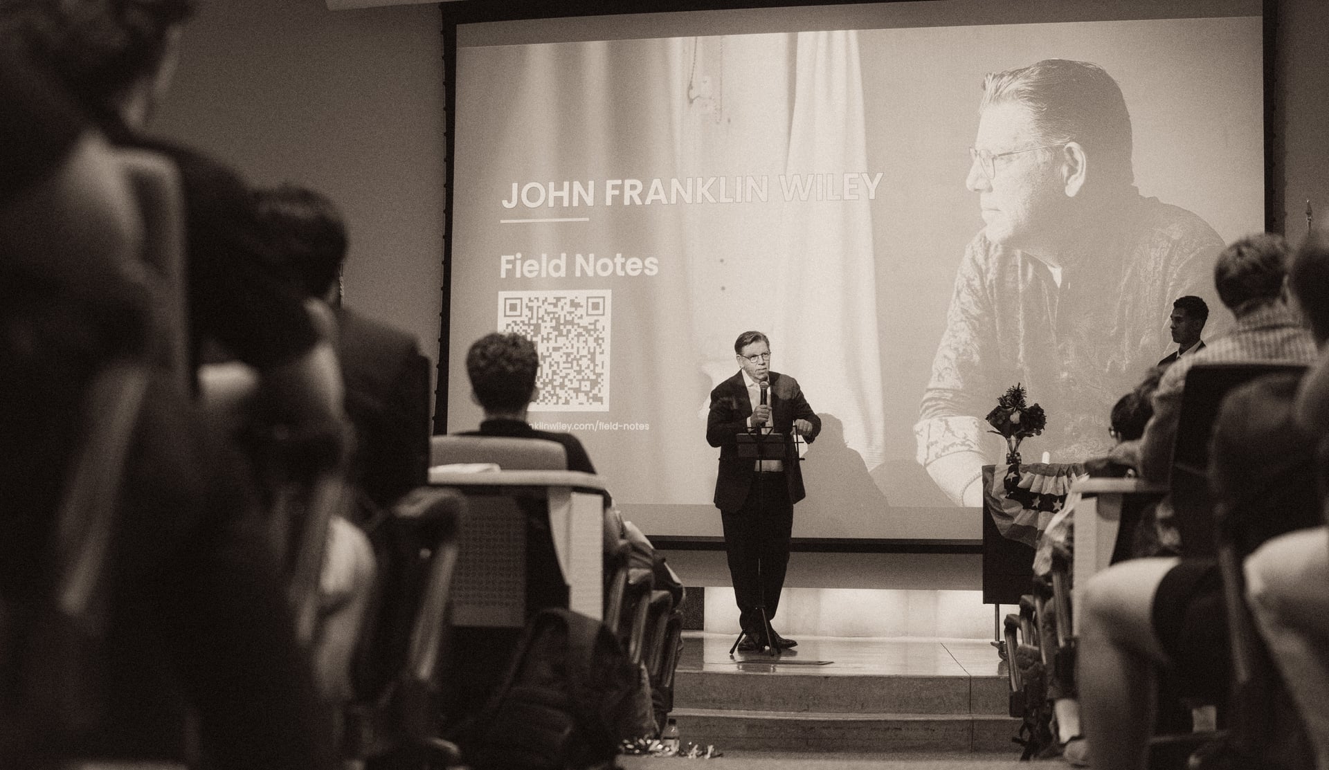John Franklin Wiley on stage at American Legion Arizona Boys State opening night, with projected speaker slide showing his name and Field Notes QR code, University of Arizona, May 31, 2026